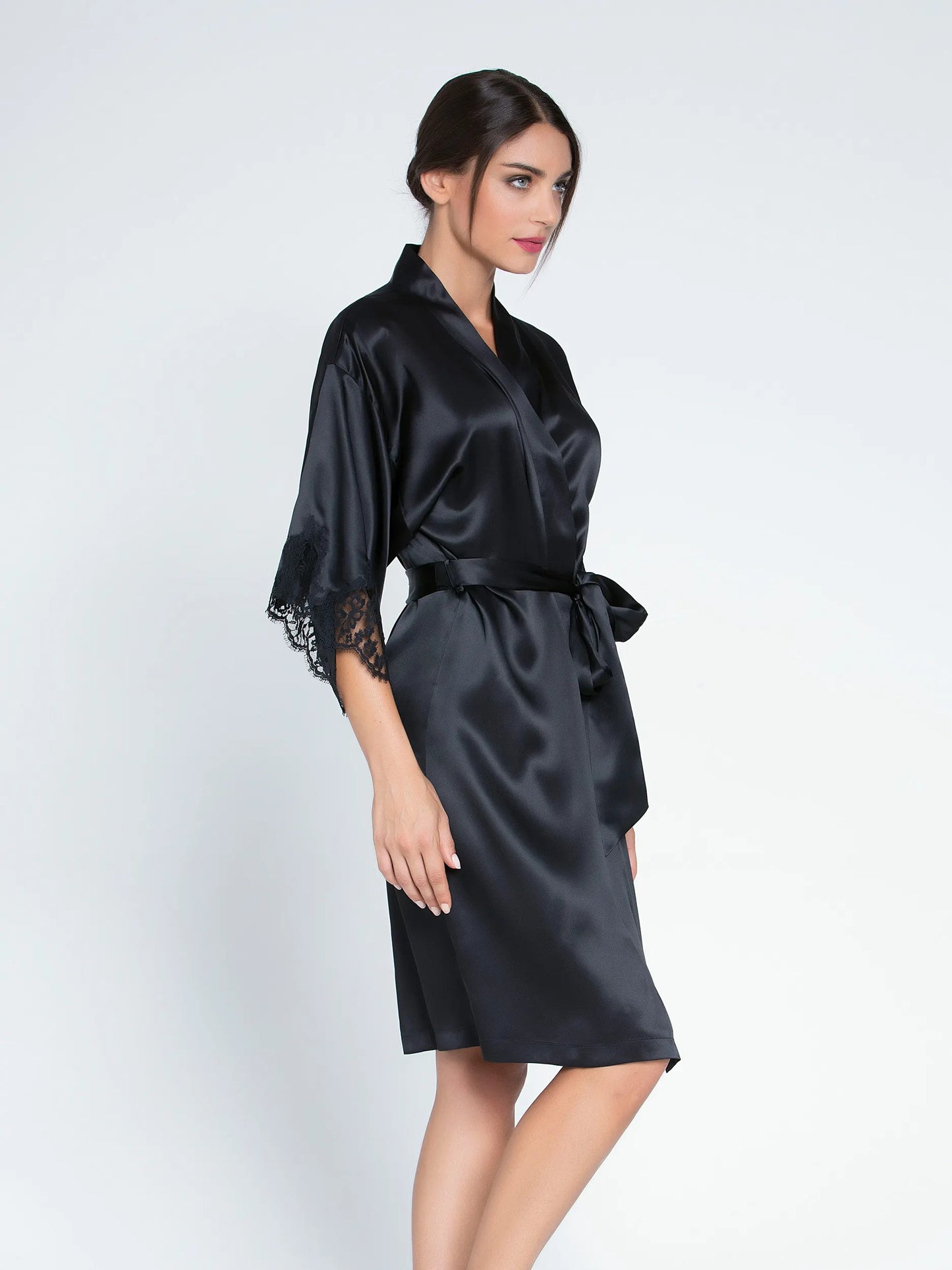 Woman wearing a black satin robe with lace cuffs on a white background