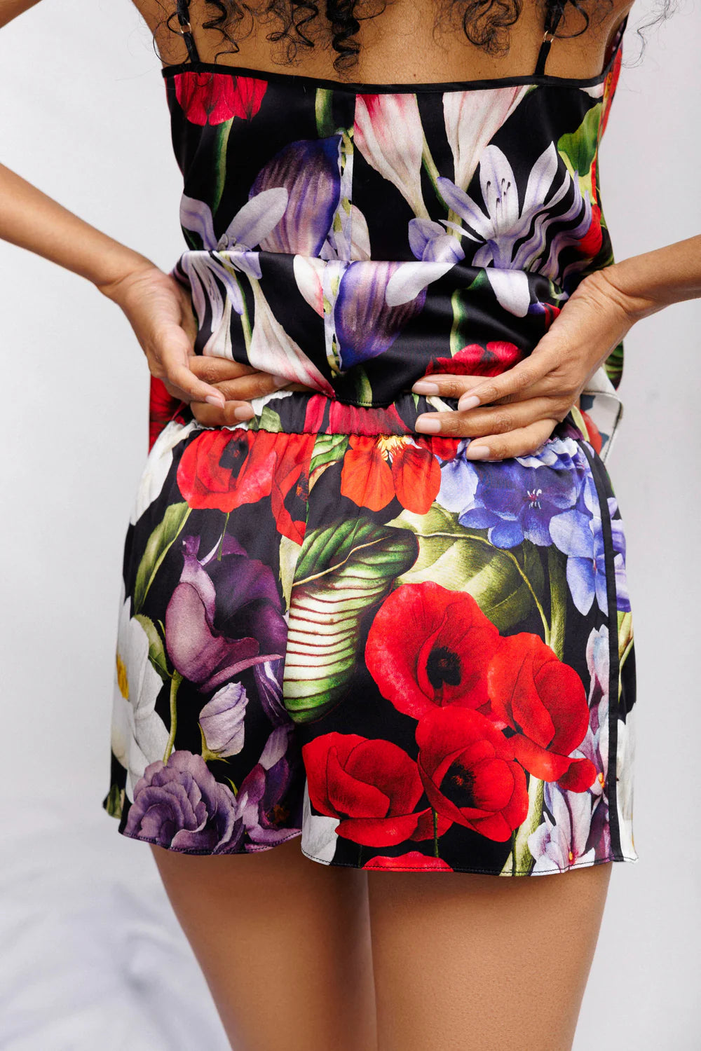 Woman wearing a colorful floral silk set of camisole and shorts. Showing the back full look.